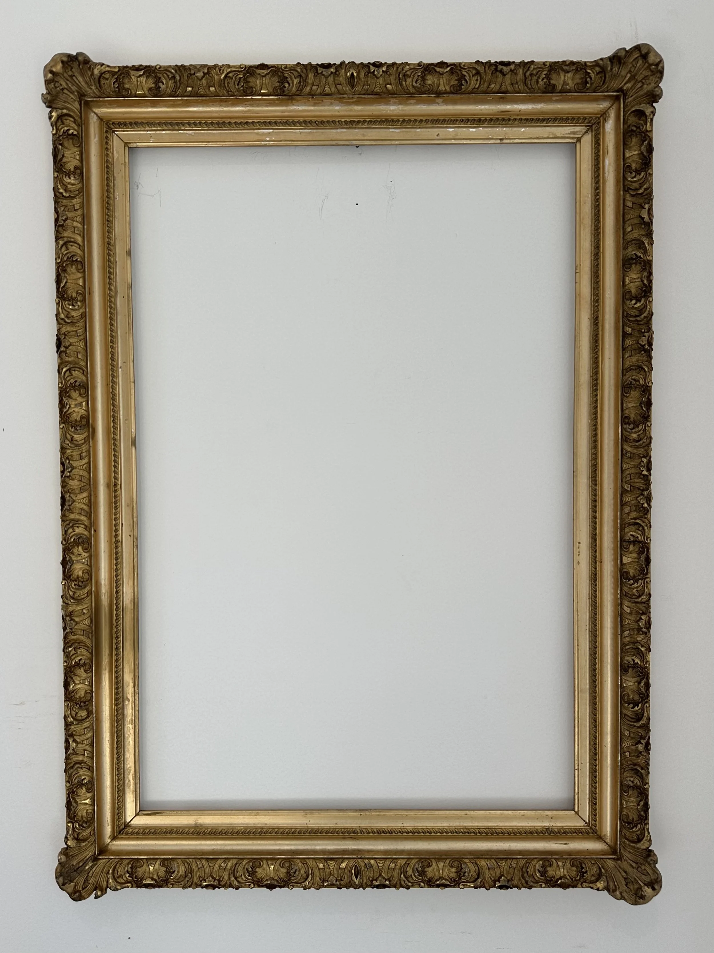 Empty ornate gold picture frame hanging on a white wall.