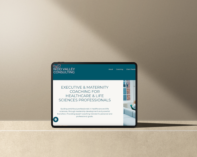 Tablet device displaying NBD Valley Consulting website with text on executive and maternity coaching for healthcare and life sciences professionals, placed on a neutral-colored surface with a plain background.