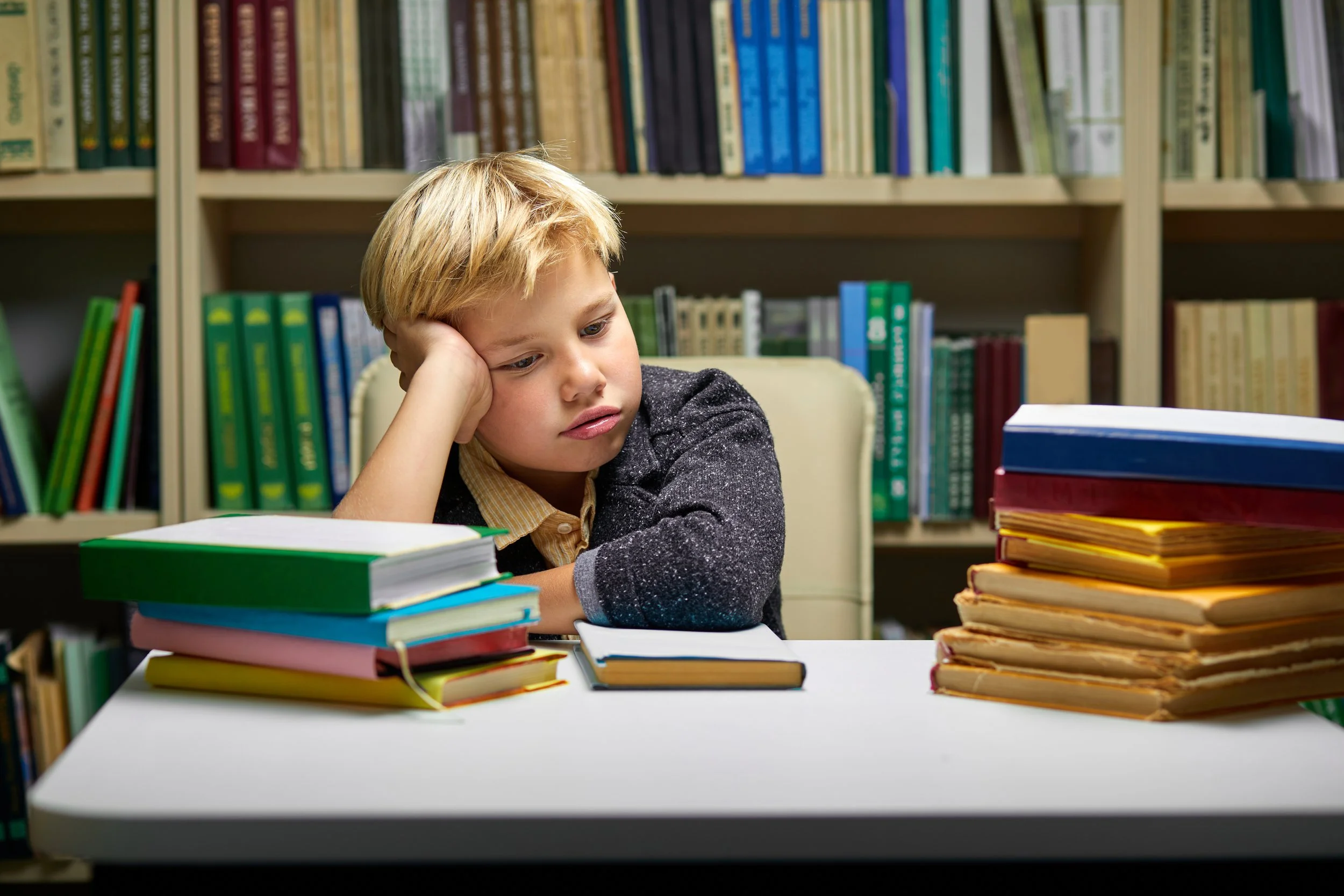A young child sitting at a desk, staring blankly at a worksheet, appearing overwhelmed
