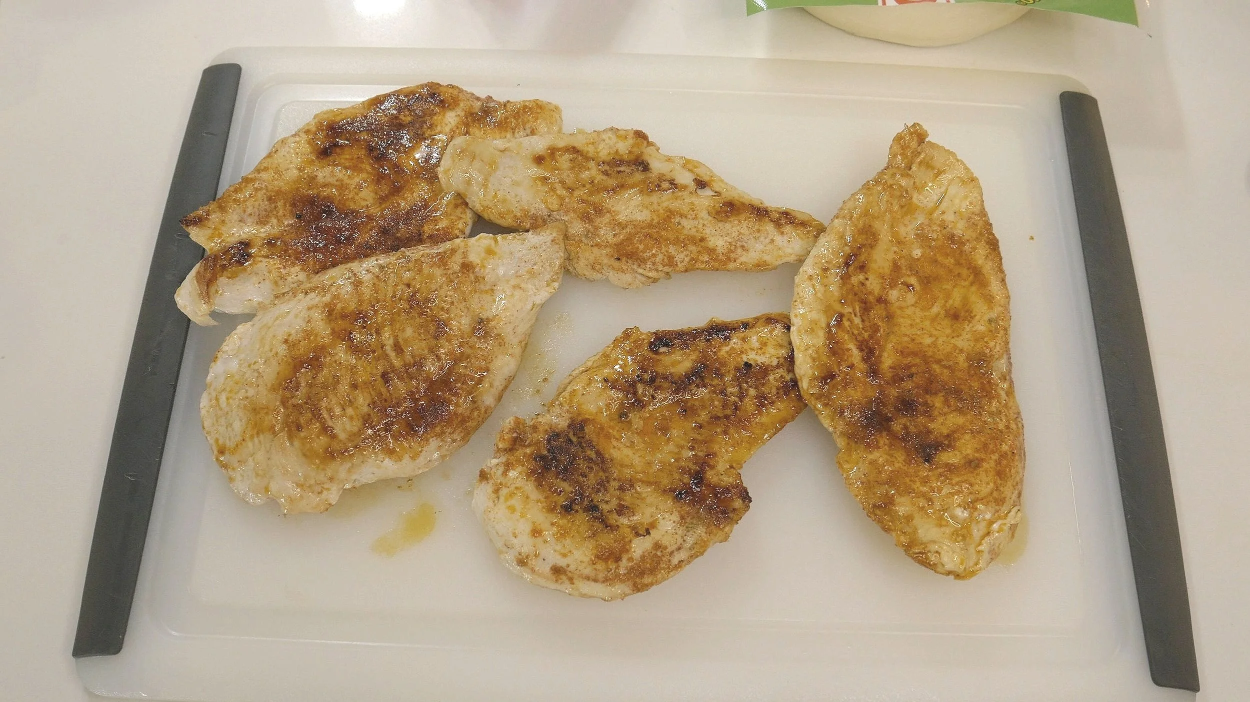 Five skillet cooked chicken breasts with golden brown smokey seasoning color resting on a white cutting board.
