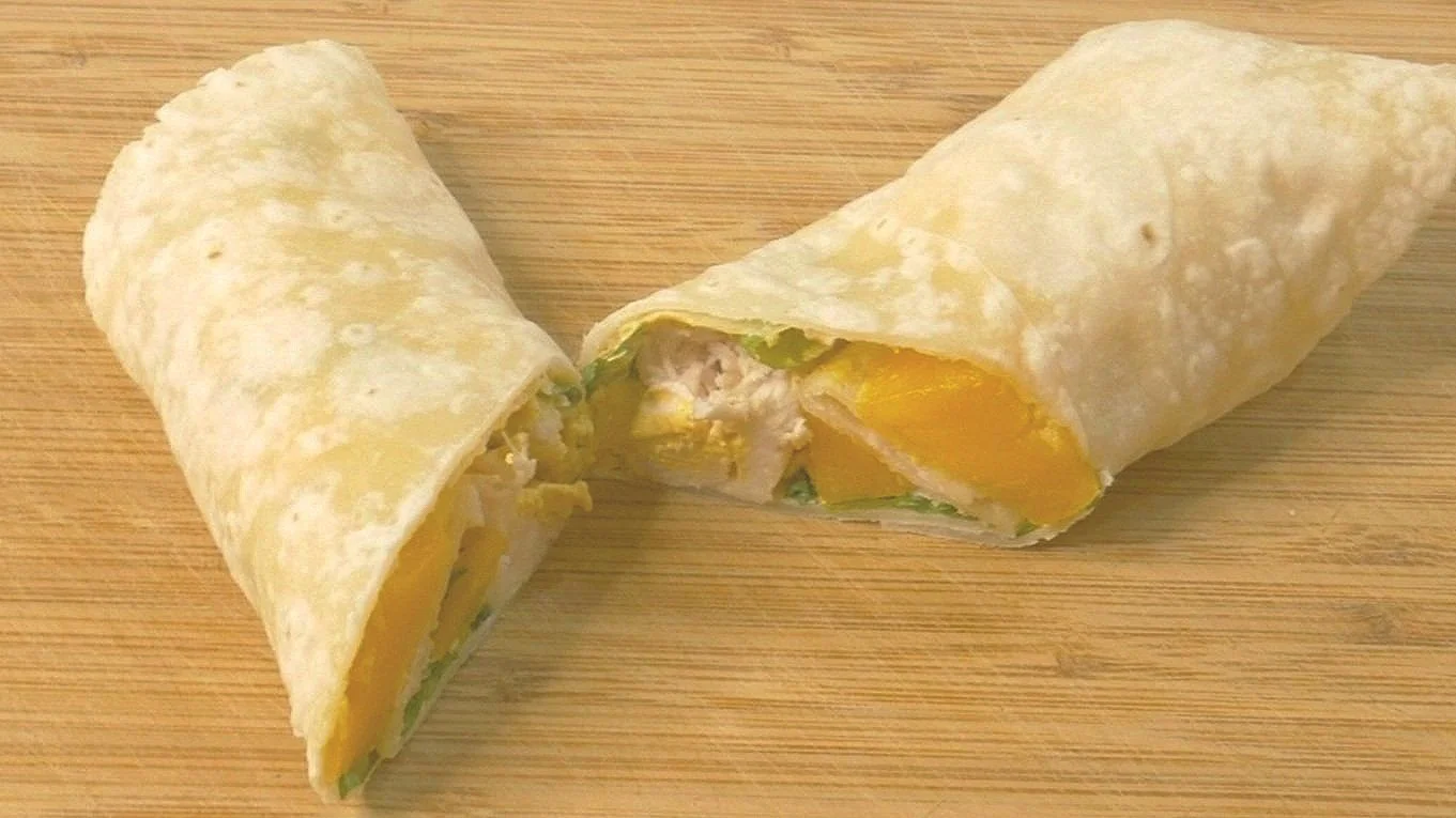 Fresh Mango and cooked chicken with freshly chopped mint and creamy curry sauce packaged in a tortilla wrap.  Sitting on a cutting board.