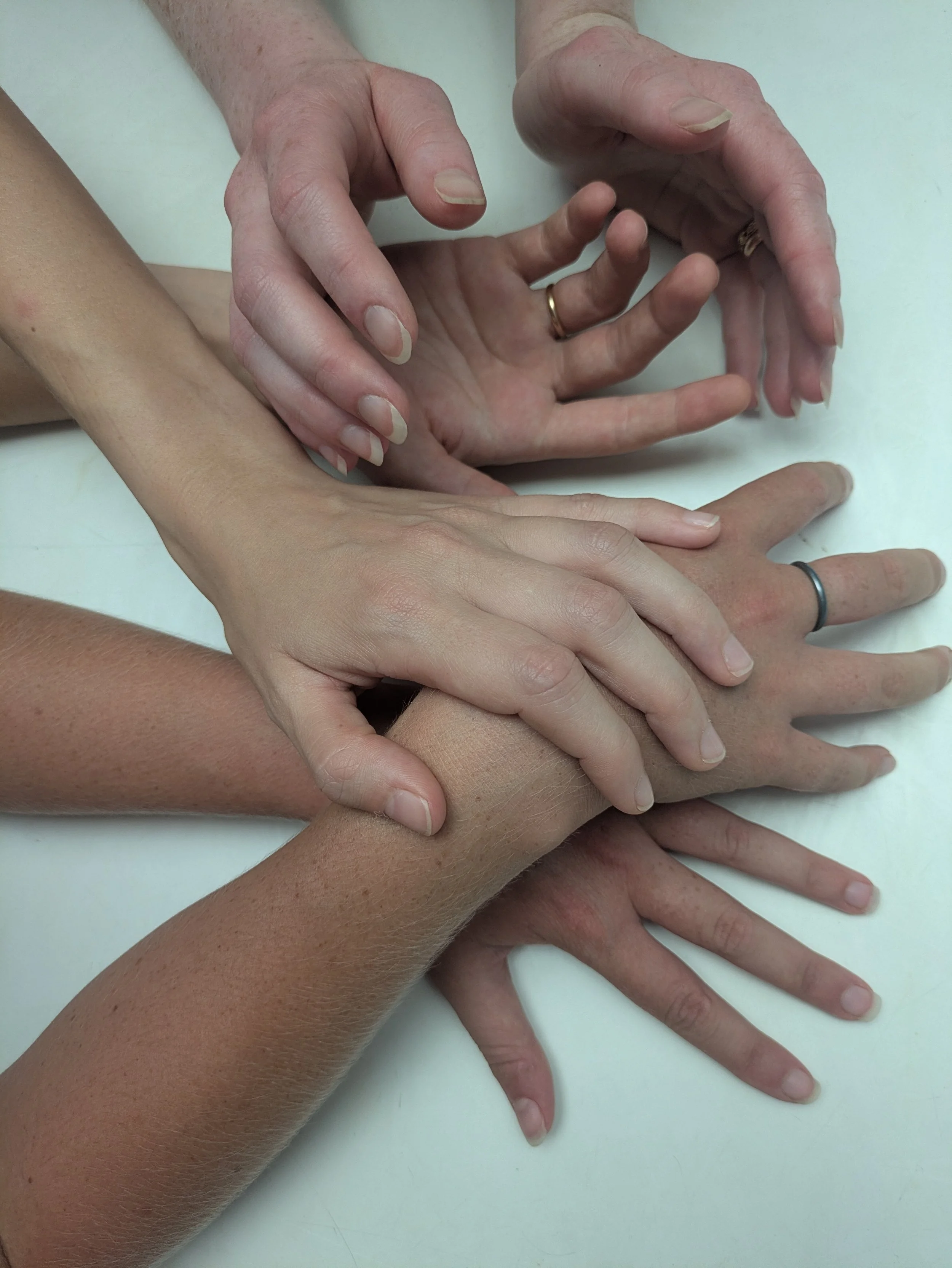 A tangle of six hands, reaching, holding, and resting, some with rings.