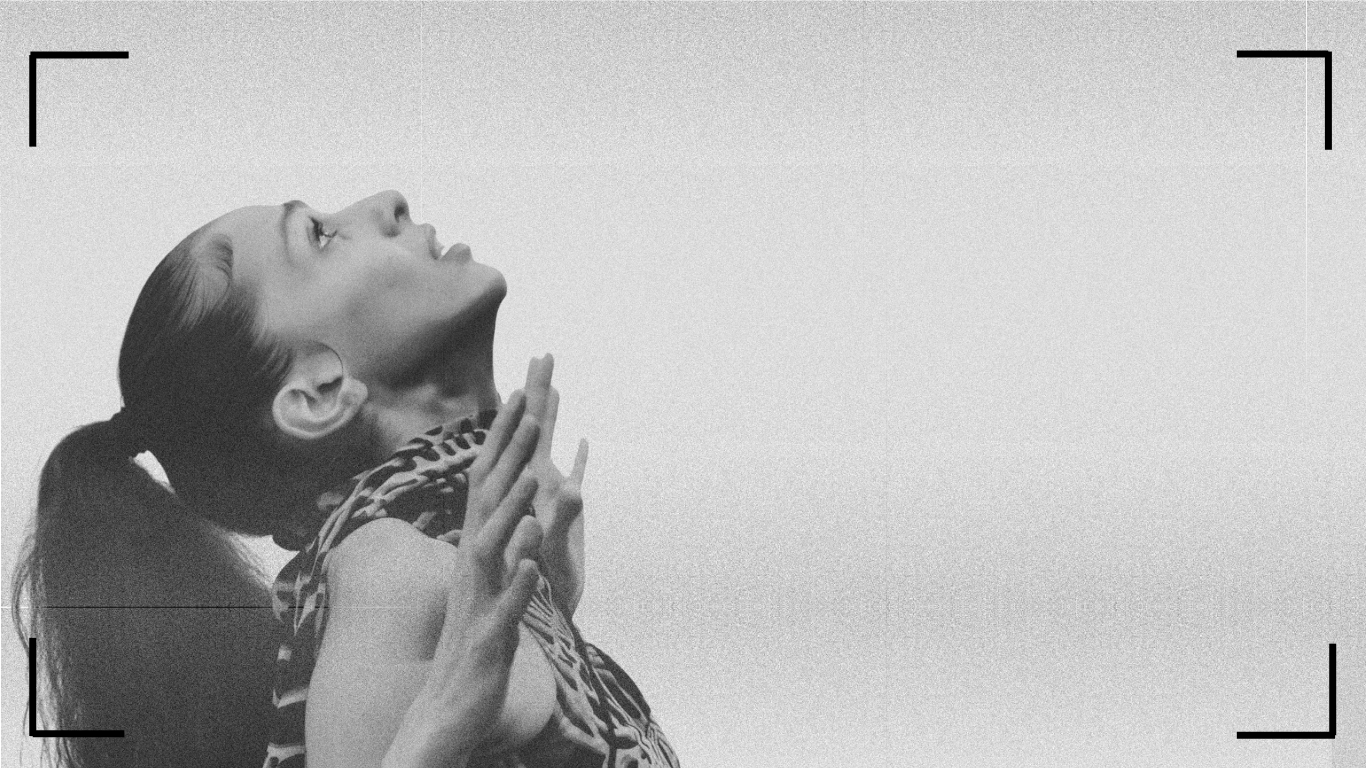 A black and white image of a woman with a ponytail looking up while holding up her hands.