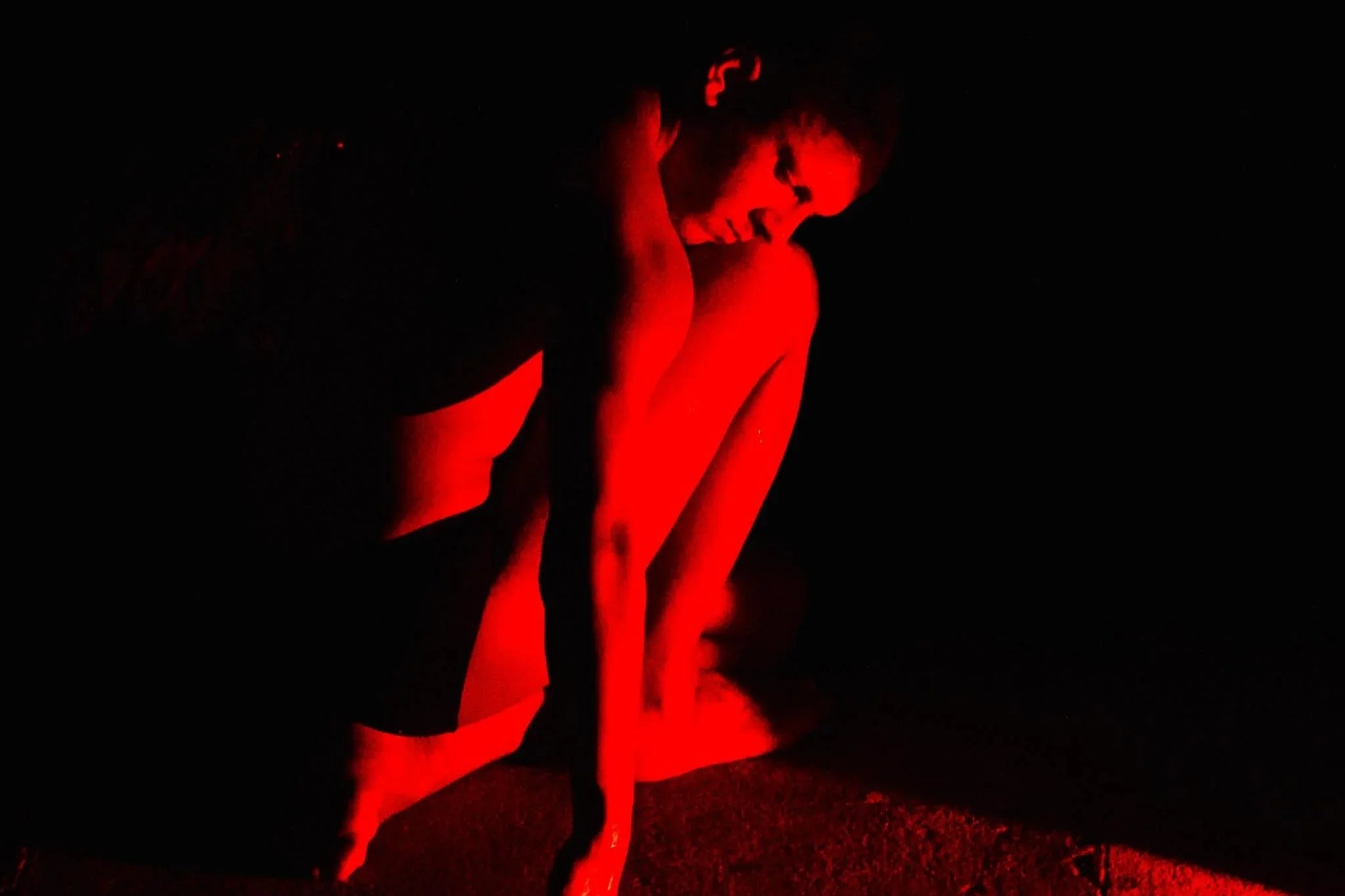 Demetris Charalambous kneels bathed in red light amidst darkness.