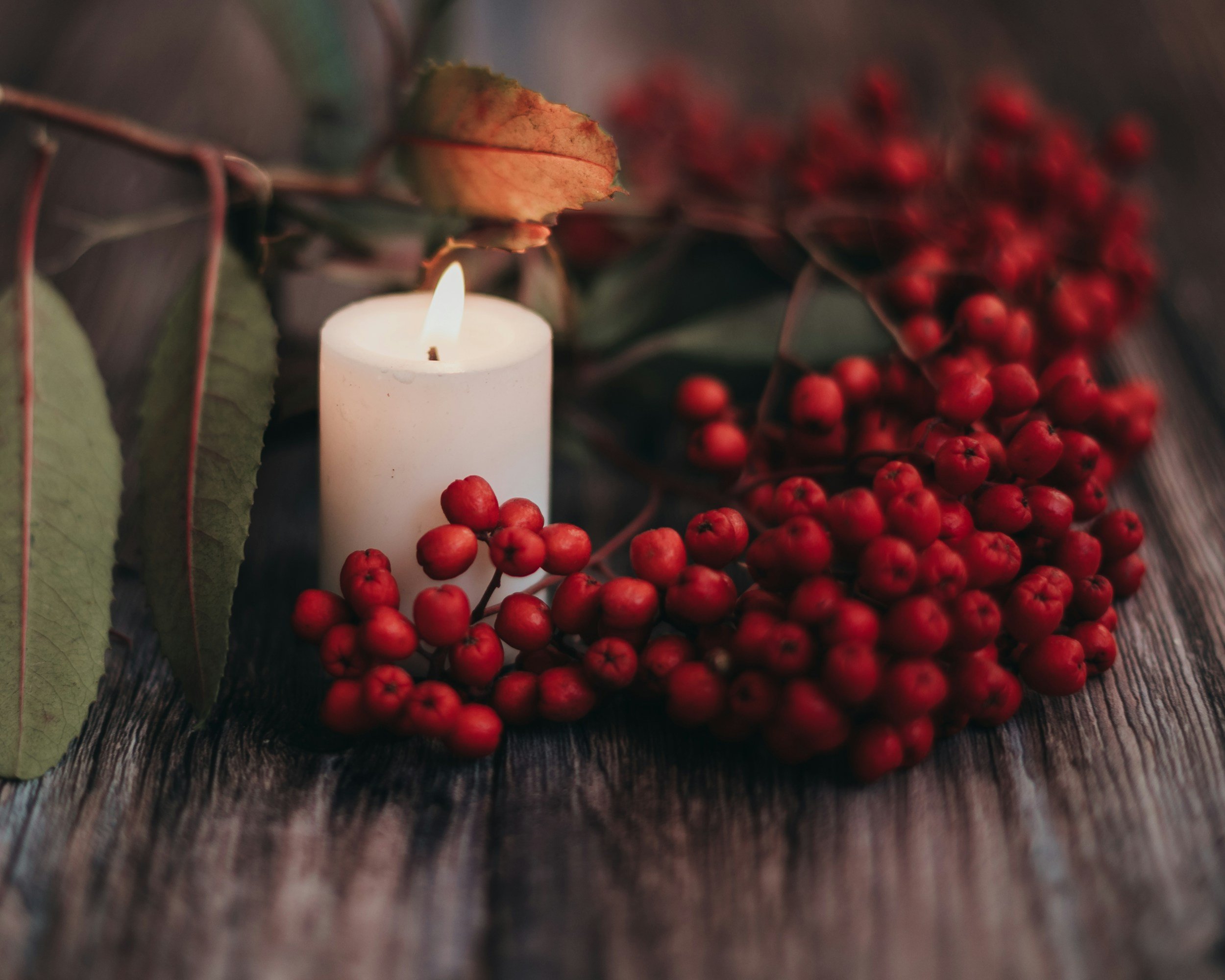 white candle, green holly leaves, and red holly berries on a brown wooden surface