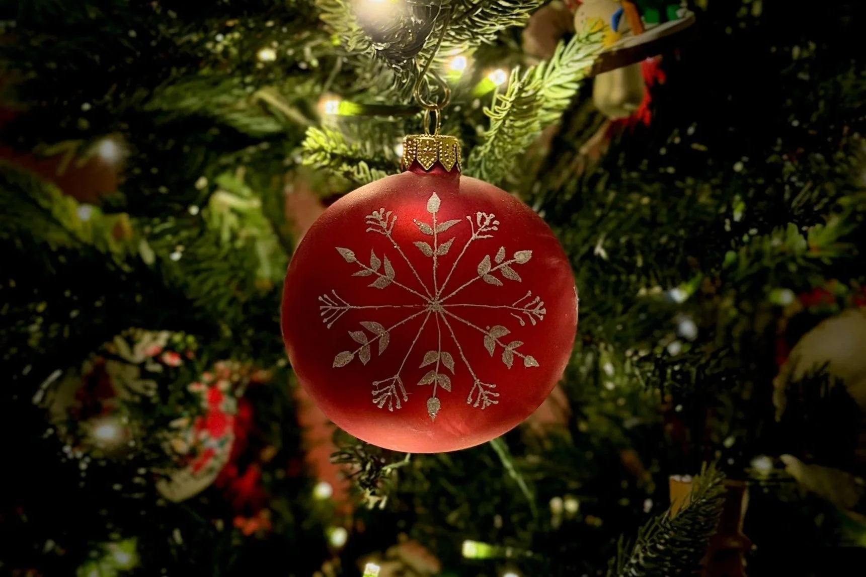 red christmas ornament with gold glitter snowflake hanging on a  Christmas tree