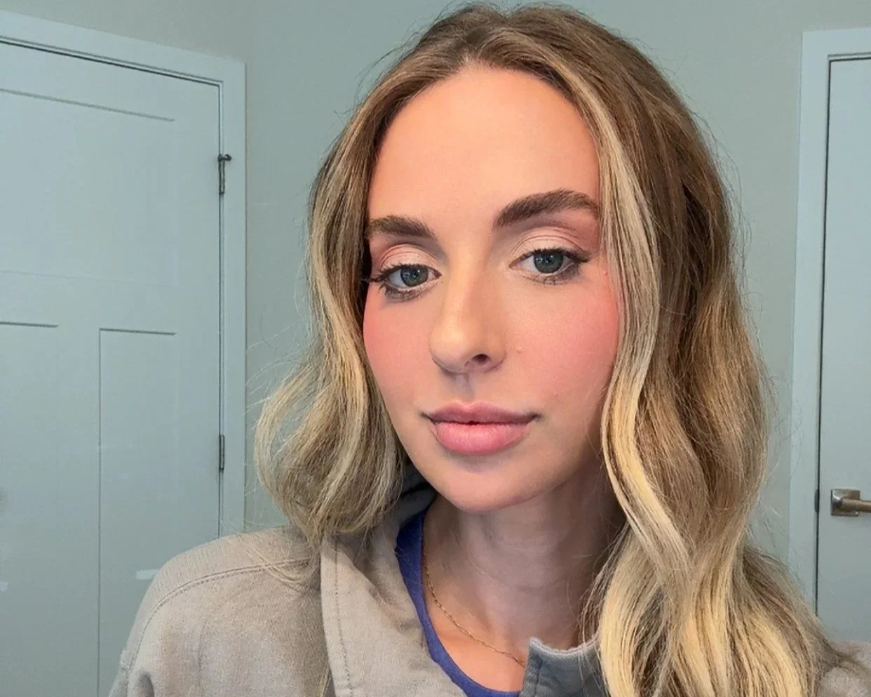 woman with wavy blonde hair wearing natural makeup in a beige room with white doors