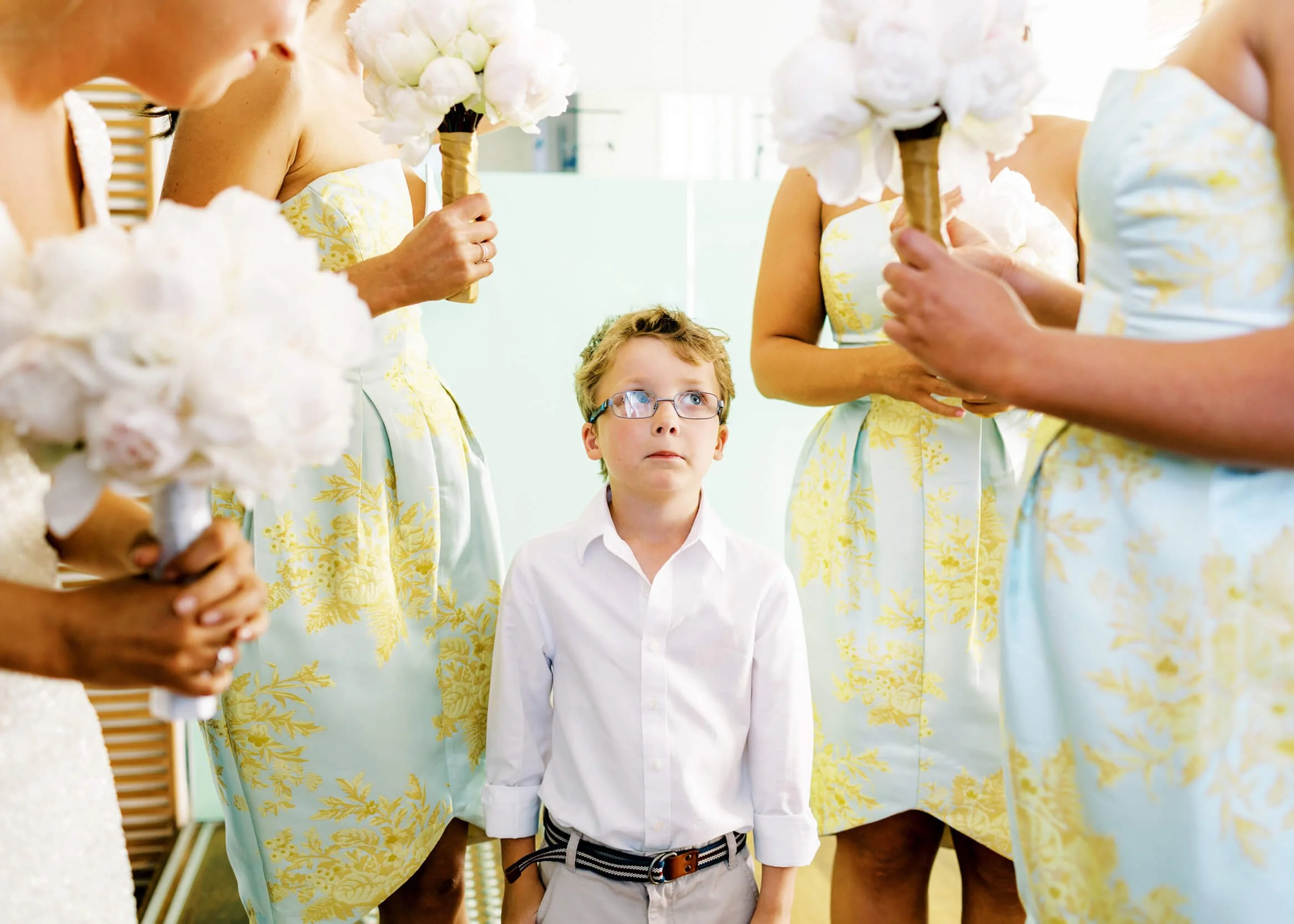 A young boy stands naturally among bridesmaids carrying pale flower bouquets during a wedding.