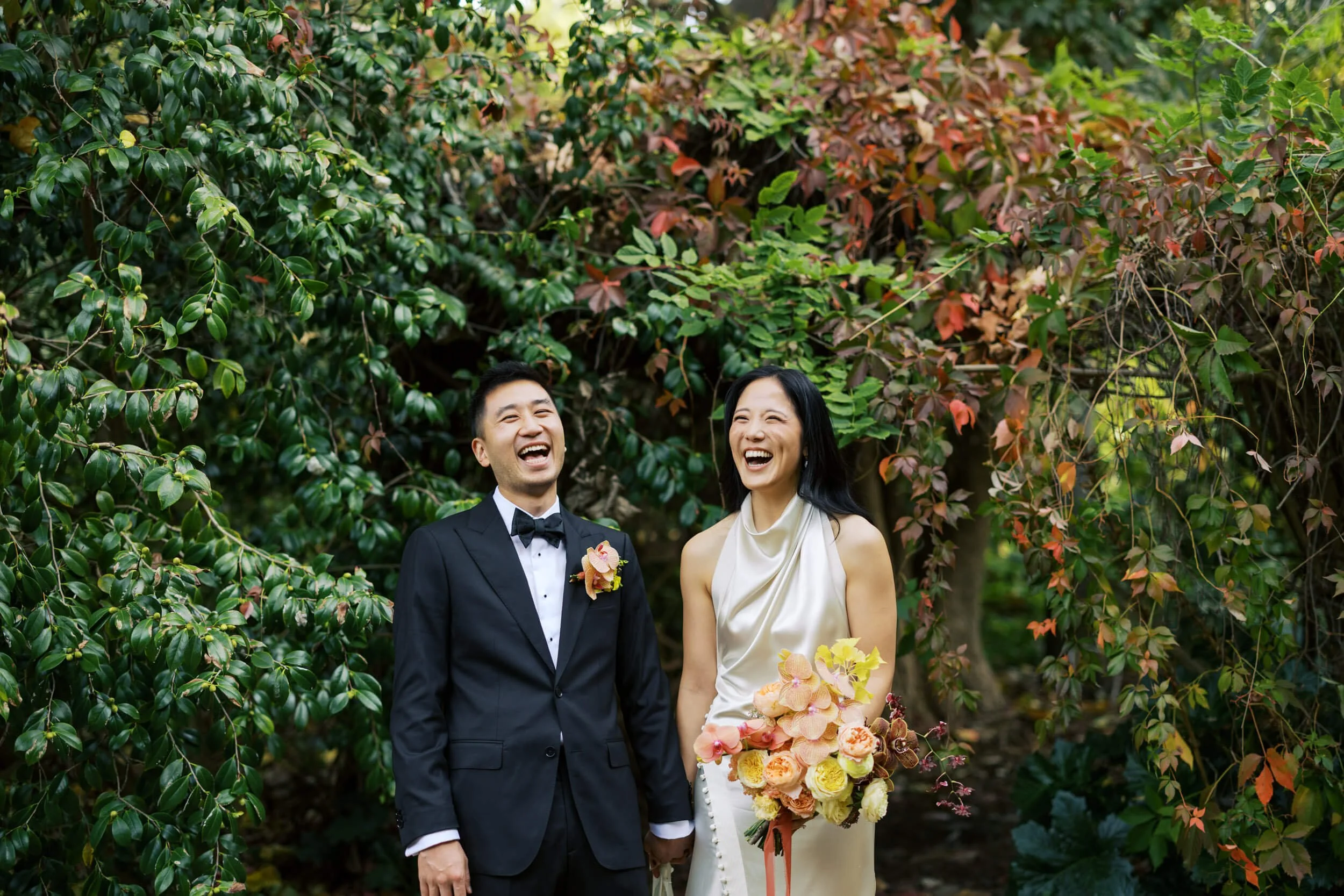 A couple share a laugh together among lush greenery at their Gardens House wedding in Melbourne.