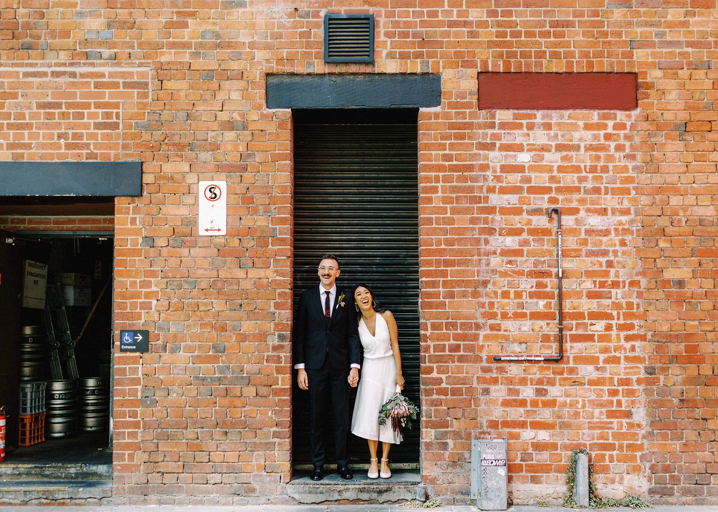 A couple share a heartfelt laugh together in the doorway of a brick building in one of Melbourne's laneways.