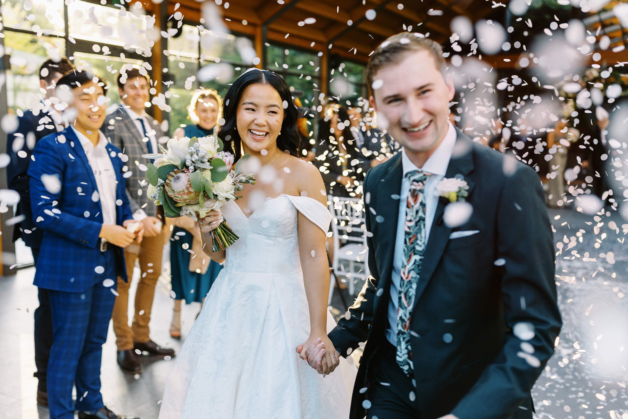 A candid moment of the bride and groom walking through a shower of confetti surrounded by smiling wedding guests at Marnong Estate