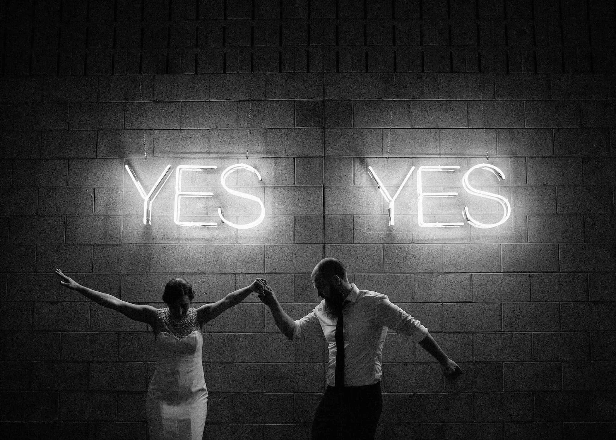 A couple dance beneath glowing neon signs in a candid black-and-white wedding photograph.