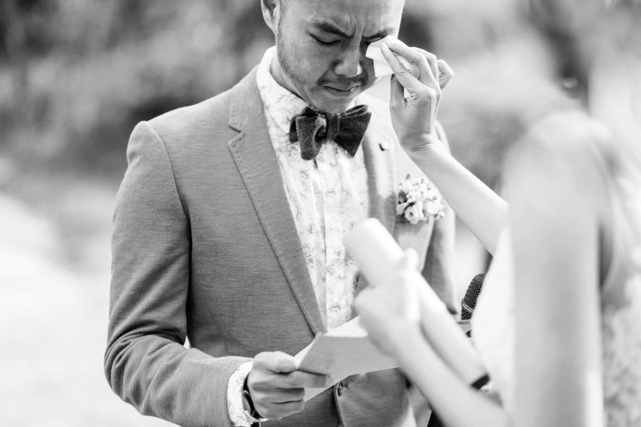 A bride wipes away a tear as the groom reads during an emotional wedding moment.