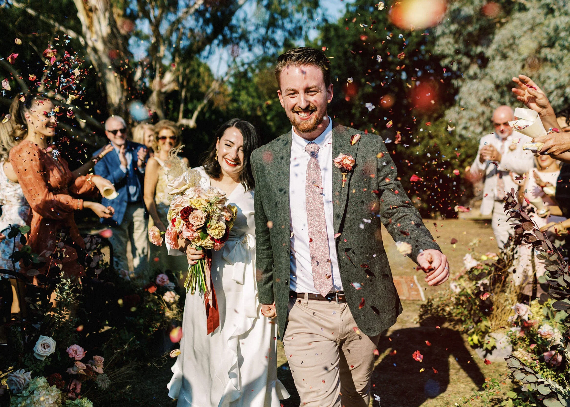 A canid moment of a couple walking through a shower of confetti surrounded by wedding guests and flowers at The Farm in Yarra Valley.