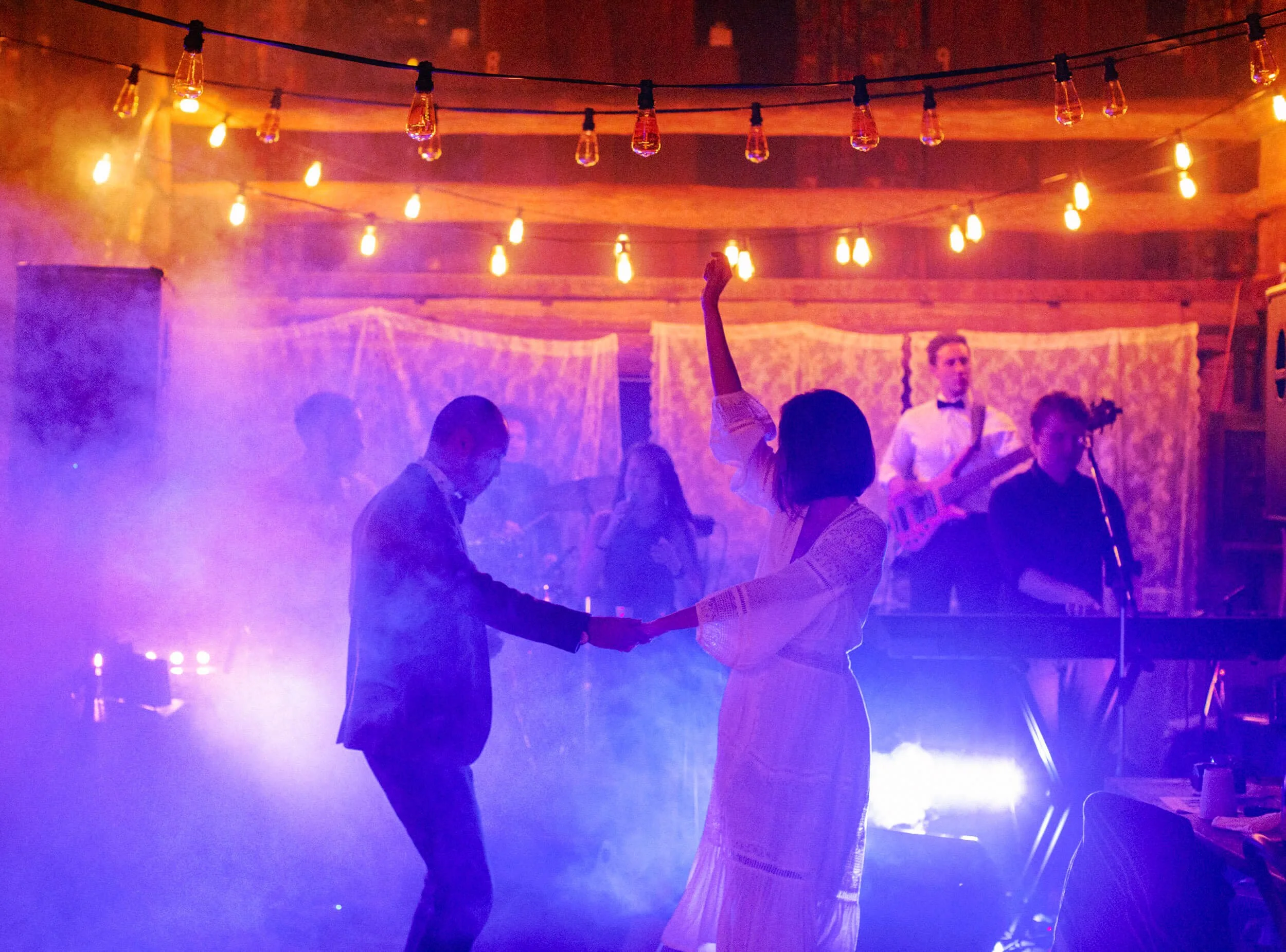 A couple dance together beneath colourful lights and haze during their wedding reception.