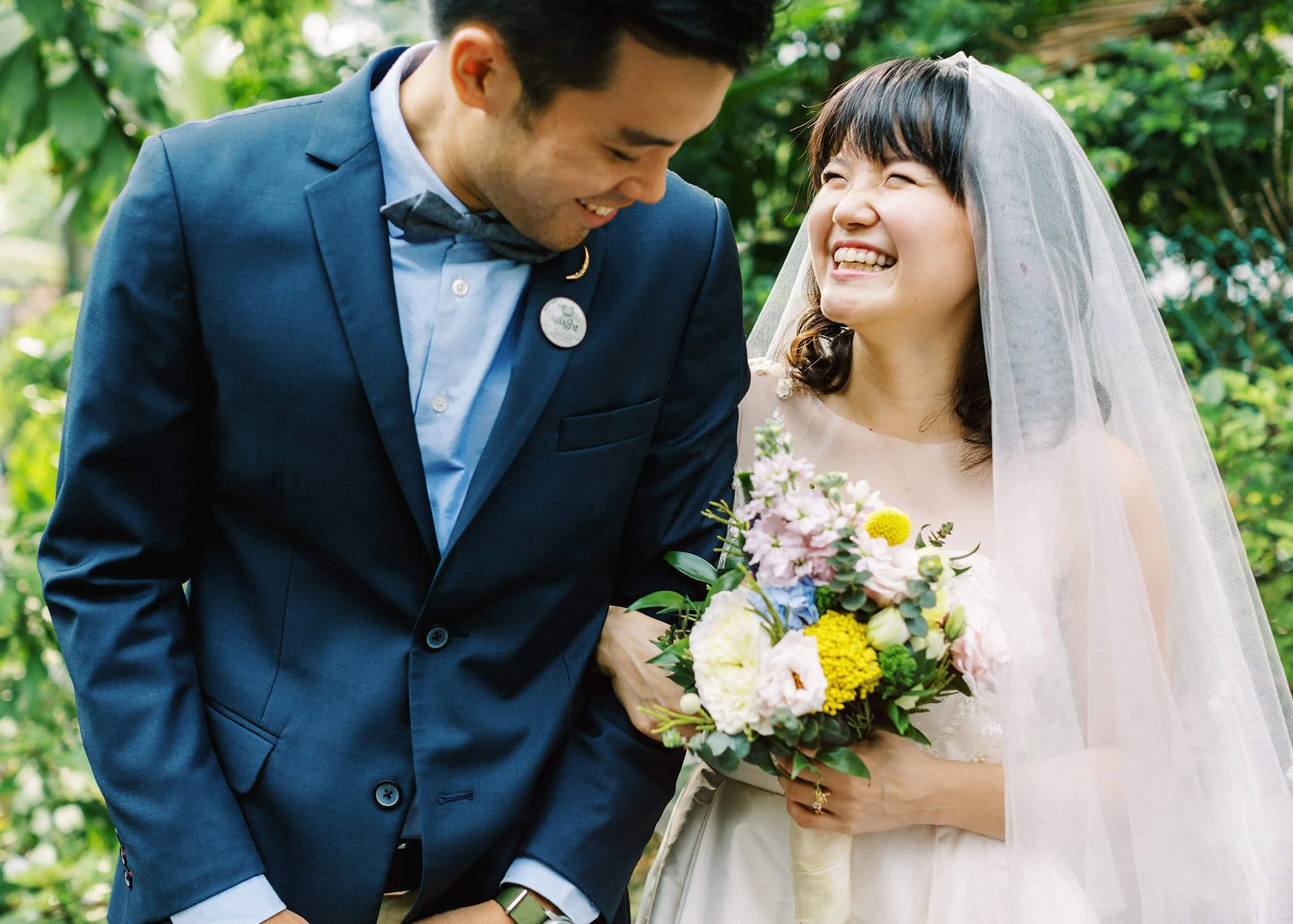 A bride and groom share a warm laugh together in a leafy garden