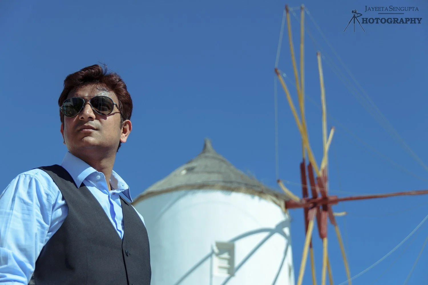 man standing near white windmill houses church bell towers blue domes oia imerovigli firostefani fira village santorini greece caldera volcanic island