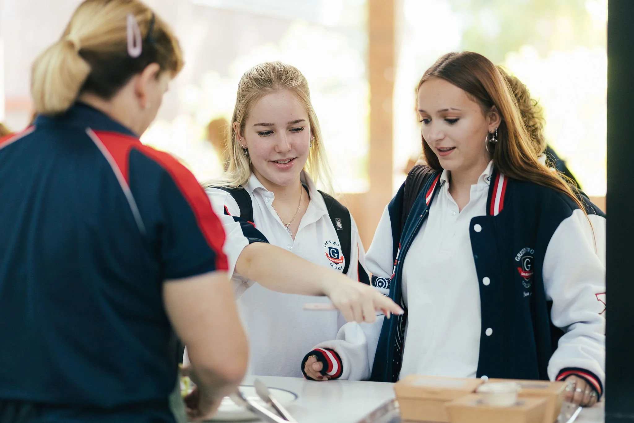 Three girls in school uniforms look at a tablet or phone together during a school event or project.