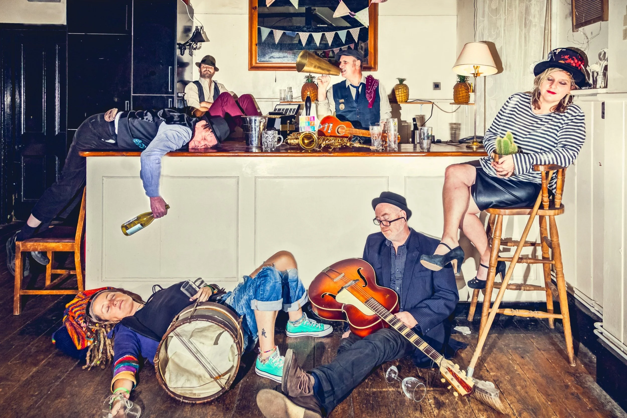 Picture of Gypskazz band (6 members) in a house bar, lying down on the floor with their instruments and bottles. Looking like a painting/ showing a story