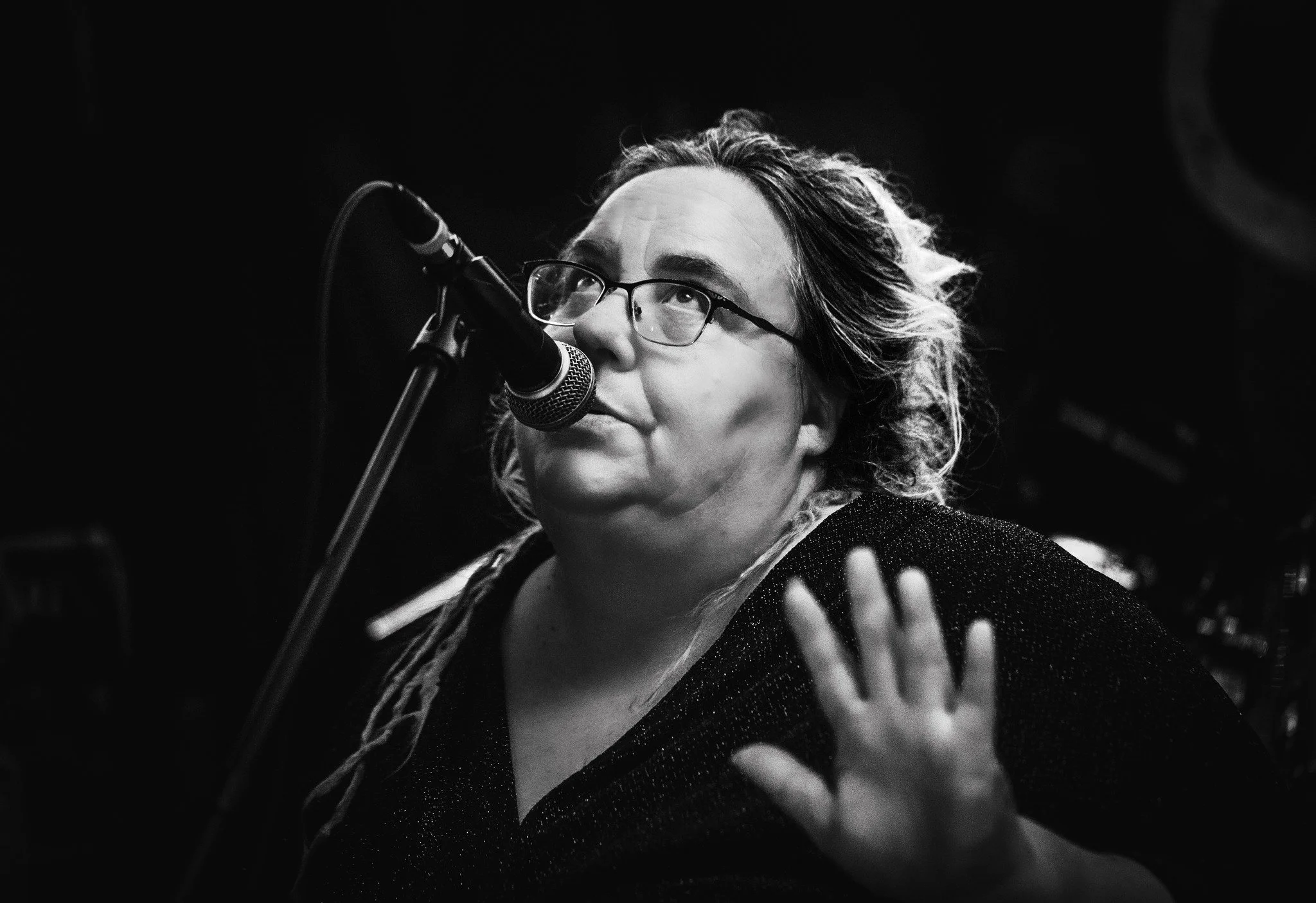 Picture of lead singer of Tarantism, Mel Rogers, in black and white - singing to a mic, one hand up, looking up