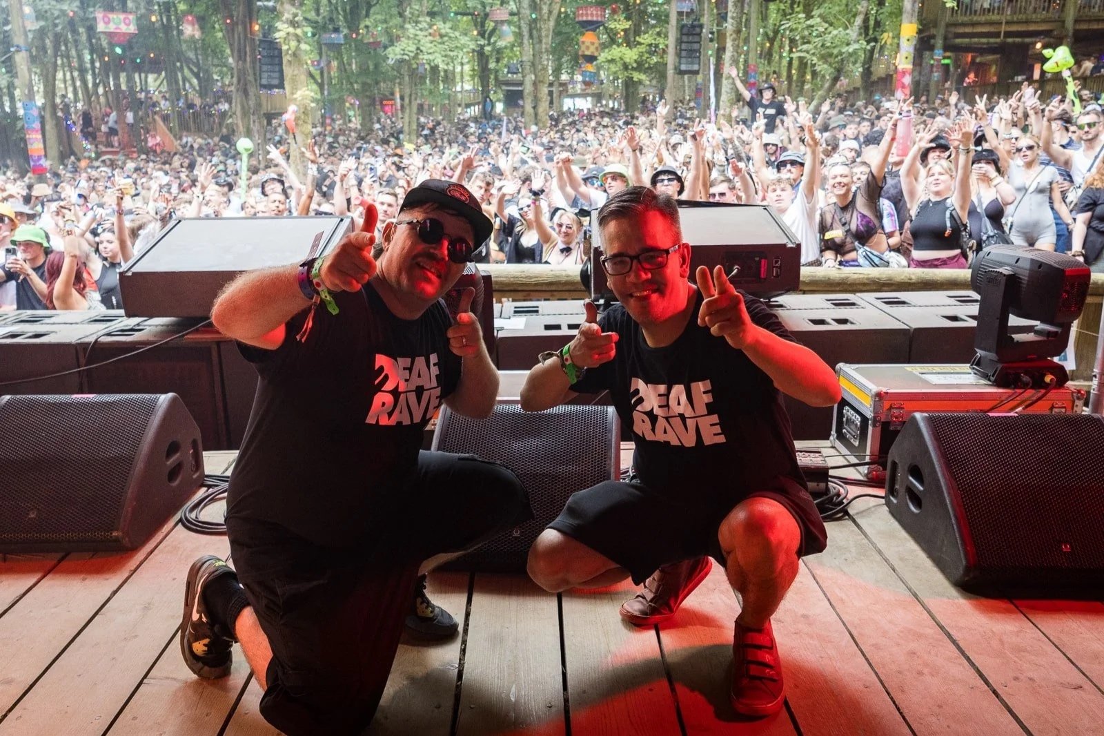 Picture of 2 members of Deaf Rave (DJ and MC) kneeling down on stage and doing a peace sign, with a full crowd behind