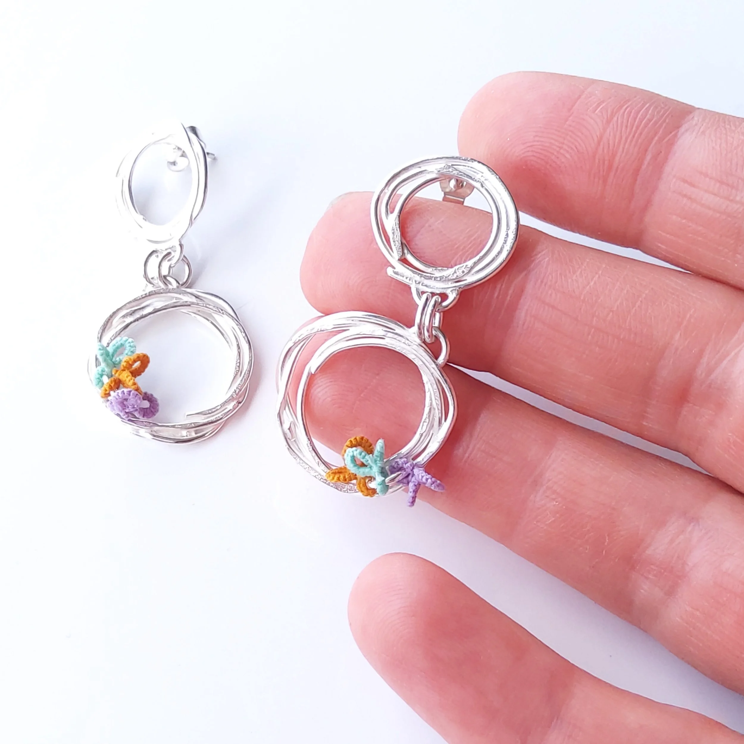 Close-up of a person's fingers holding a silver bracelet with colorful woven charms.