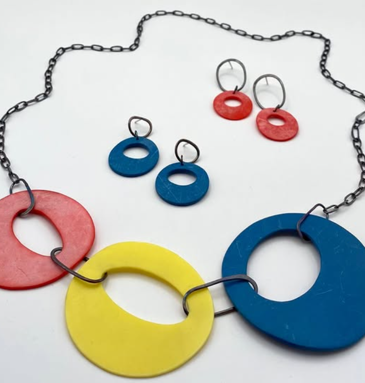 Colorful jewelry set with large circular beads in red, yellow, and blue, including a necklace and matching earrings, arranged on a white surface.