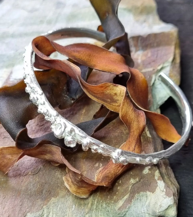 Silver headband with decorative beads resting on dried brown leaves and wood surface