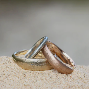 Two wedding rings, one silver and one rose gold, partially buried in sand