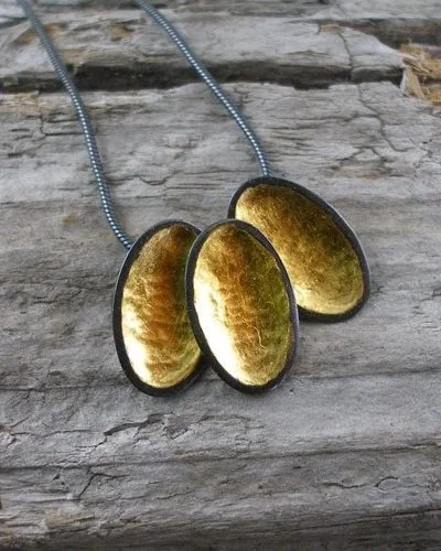 A necklace with three oval-shaped pendants featuring amber-colored, textured stones on a wooden surface.