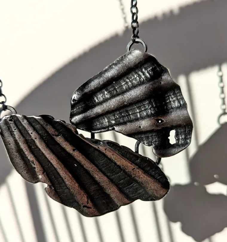 Close-up of a butterfly-shaped pendant made of black and brown textured metal, hanging from a chain.