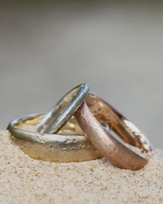 Three rusted and weathered metal rings partially buried in sand, stacked together at the beach.