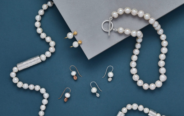 Collection of pearl jewelry including a pearl necklace, pearl bracelet, and pearl earrings, arranged on a blue surface with a gray box.