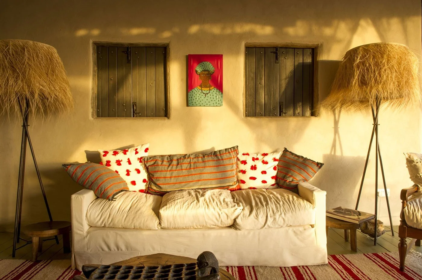 Lys sofa med mønstrede puter mellom to gulvlamper, med fargerik kunst på veggen bak.