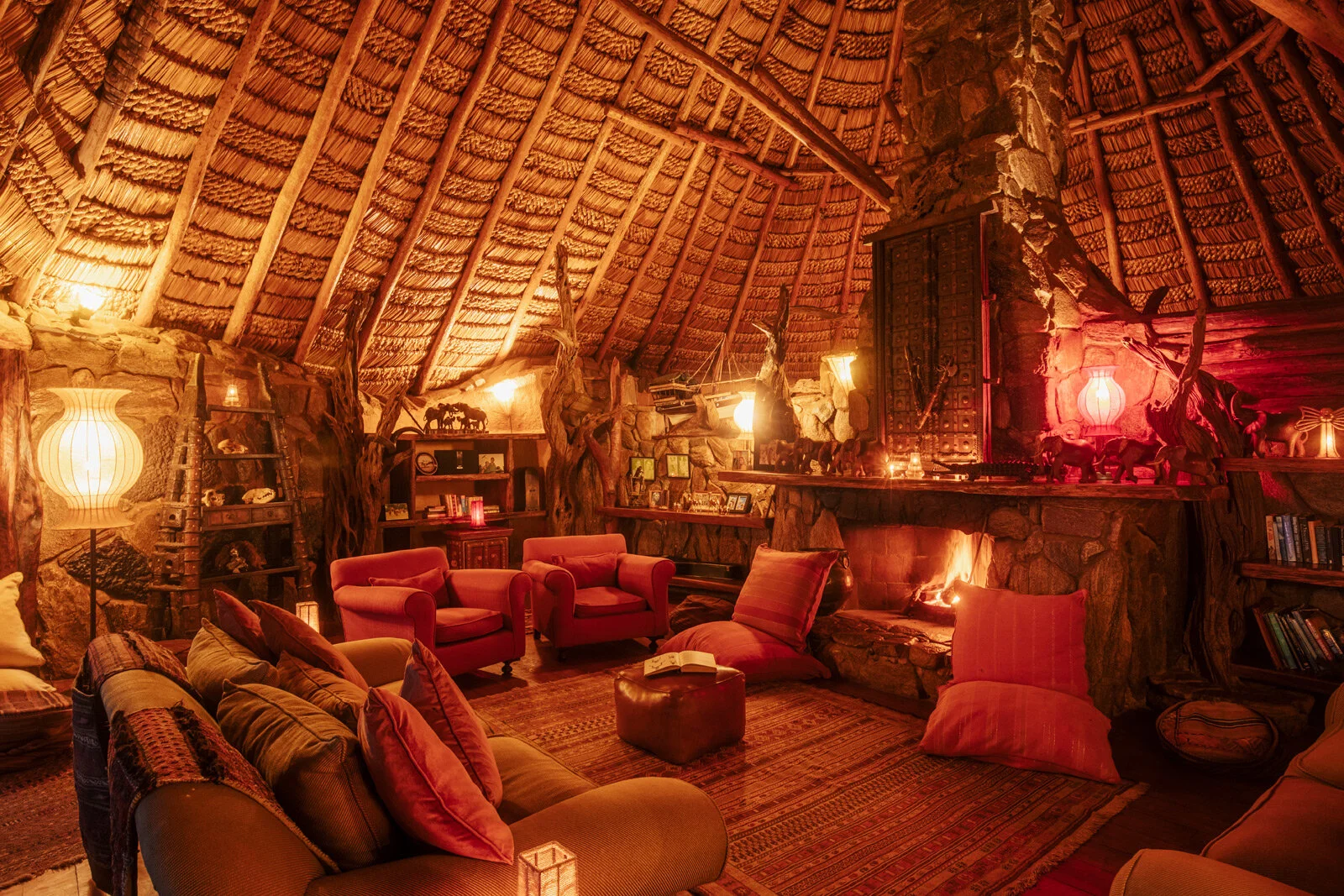 Stue med røde puter og høyt stråtak på Ol Malo Lodge, en base for luksussafari i Laikipia, Kenya.