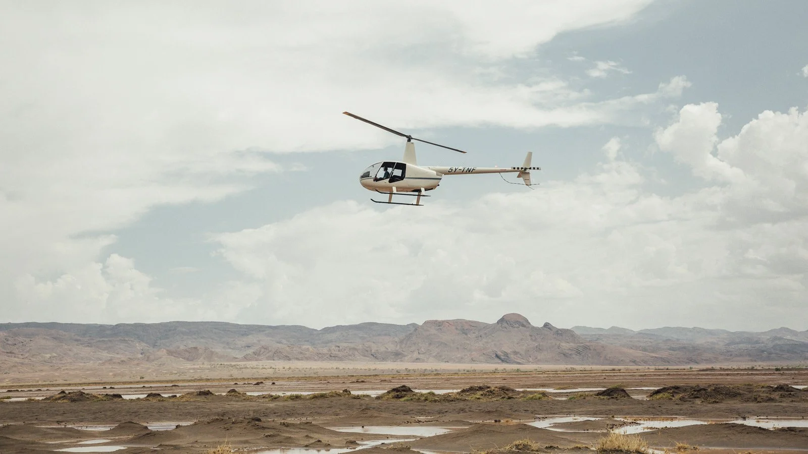 Helikopter flyr over et åpent, tørt landskap på helikoptersafari fra Ol Malo i Nord-Kenya.