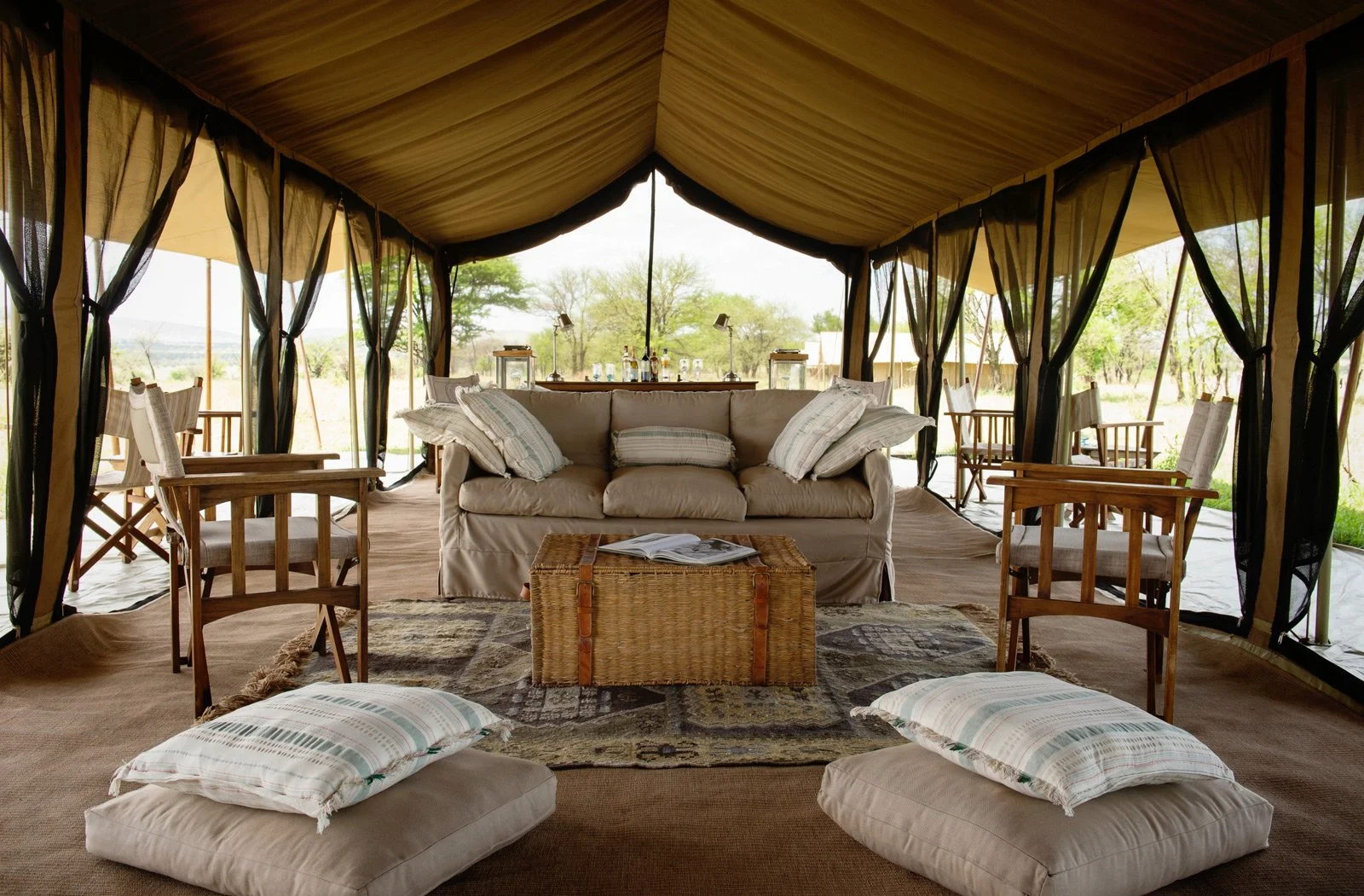 Åpent fellestelt med sofa, lenestoler og gulvputer på Serengeti Safari Camp i Tanzania.