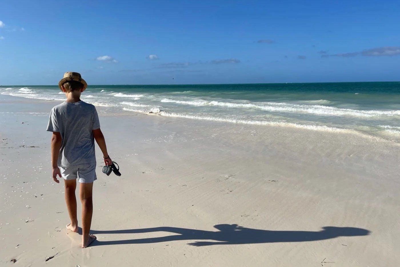 Gutt går langs strand i Afrika etter familiesafari, med hav og sand