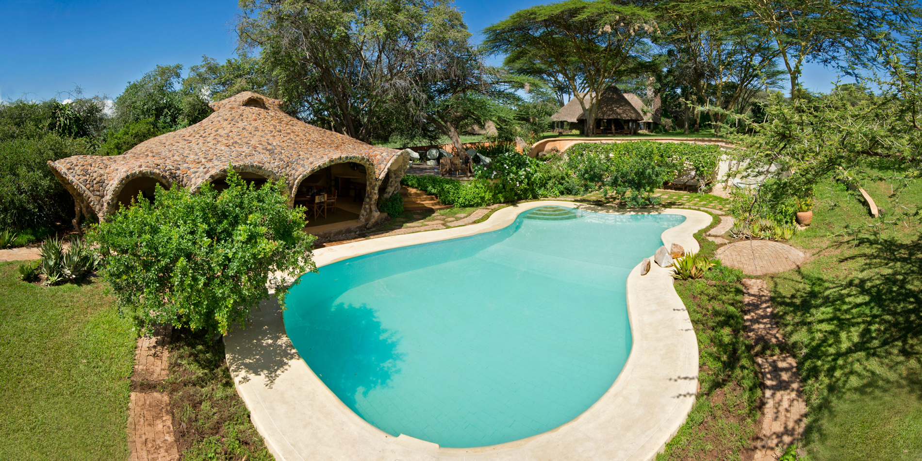 Basseng omgitt av trær og stråtekte bygninger ved Lewa House i Kenya.