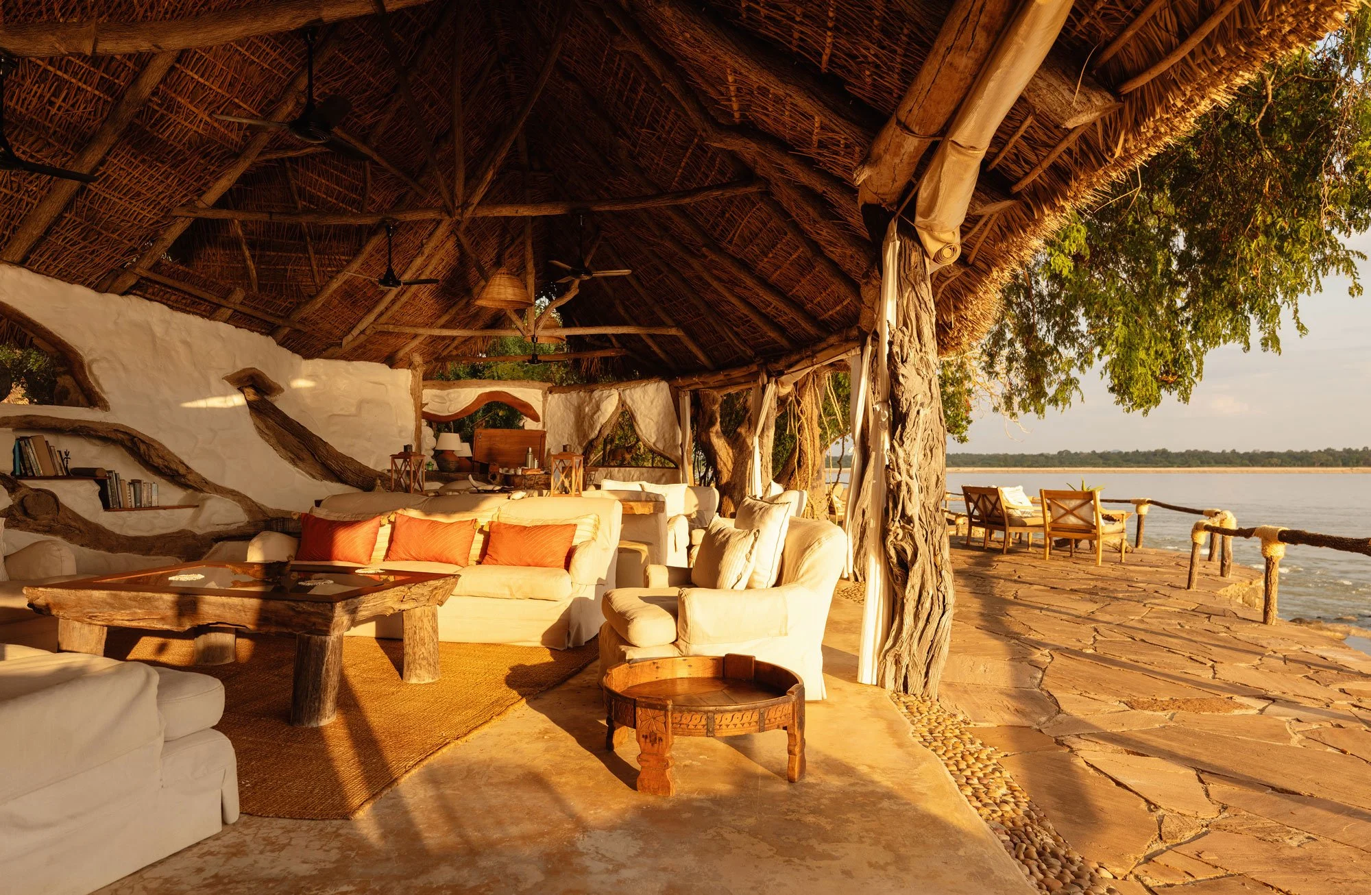 Åpen lounge med sofaer under stråtak og terrasse mot Rufiji-elven på Sand Rivers Selous.