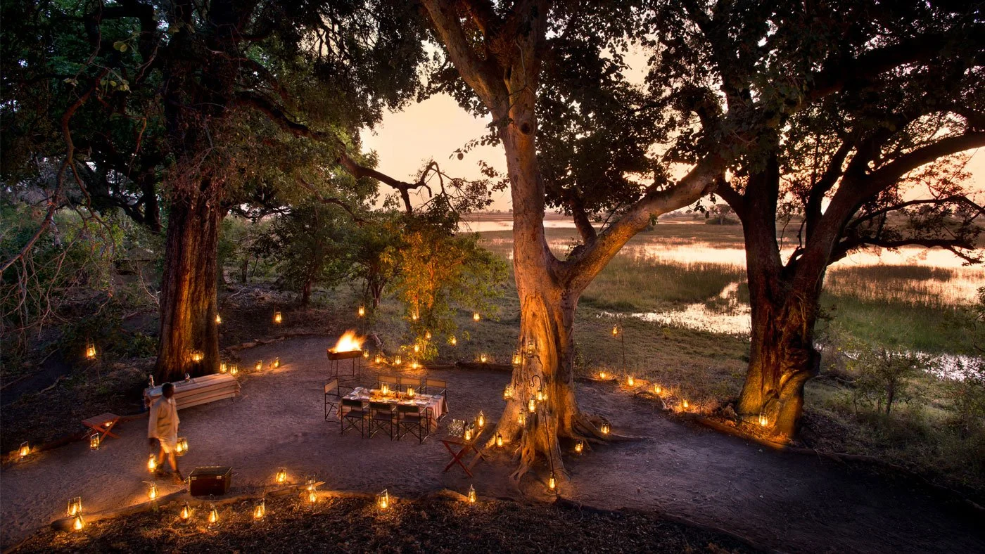 Luksus safari-lodge i Afrika med privat middag under trær ved elvebredden