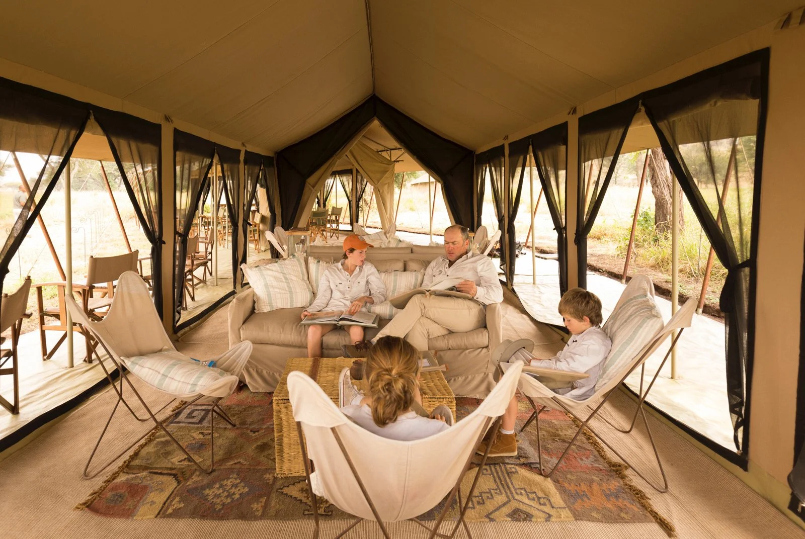 En familie sitter sammen i sofa og lenestoler i det åpne fellesteltet på Serengeti Safari Camp.