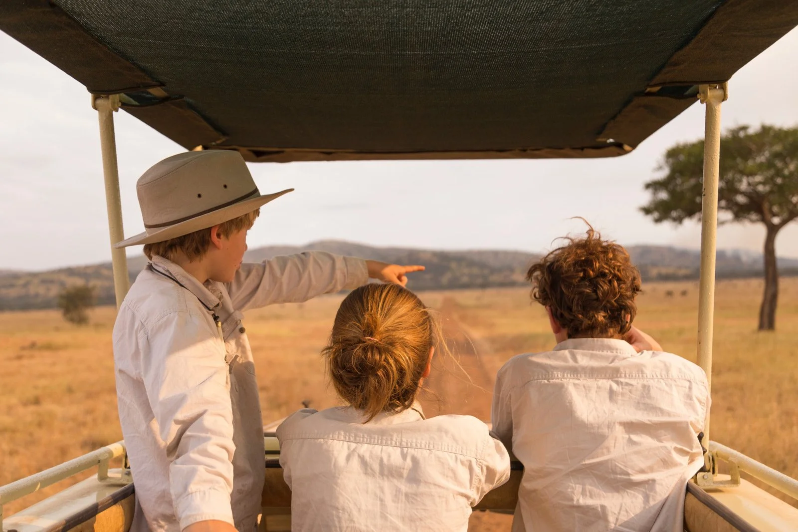 Tre barn ser utover savannen fra en safaribil, mens ett av barna peker mot noe i landskapet.