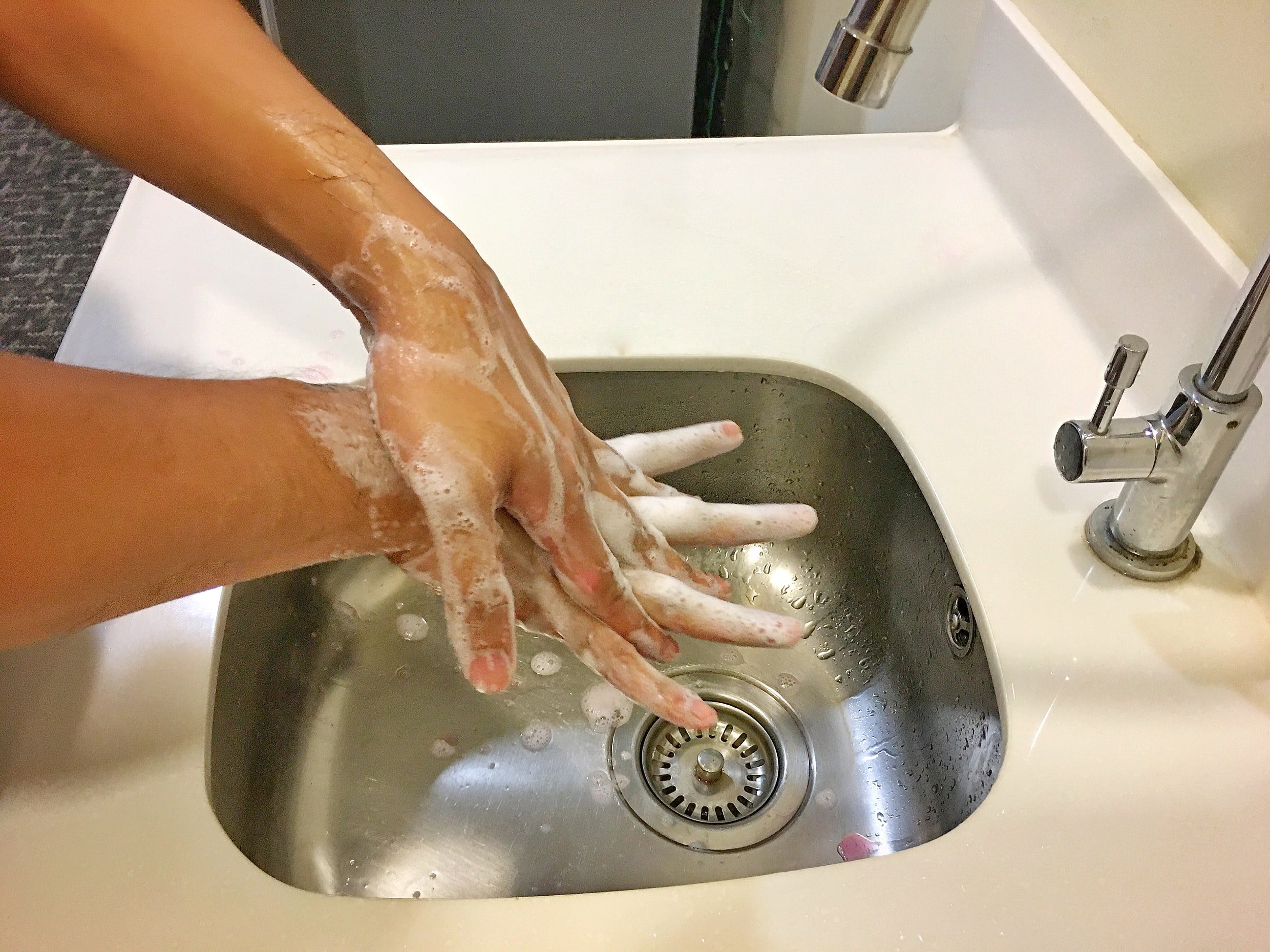 Person washing hands with soap in a stainless steel sink.