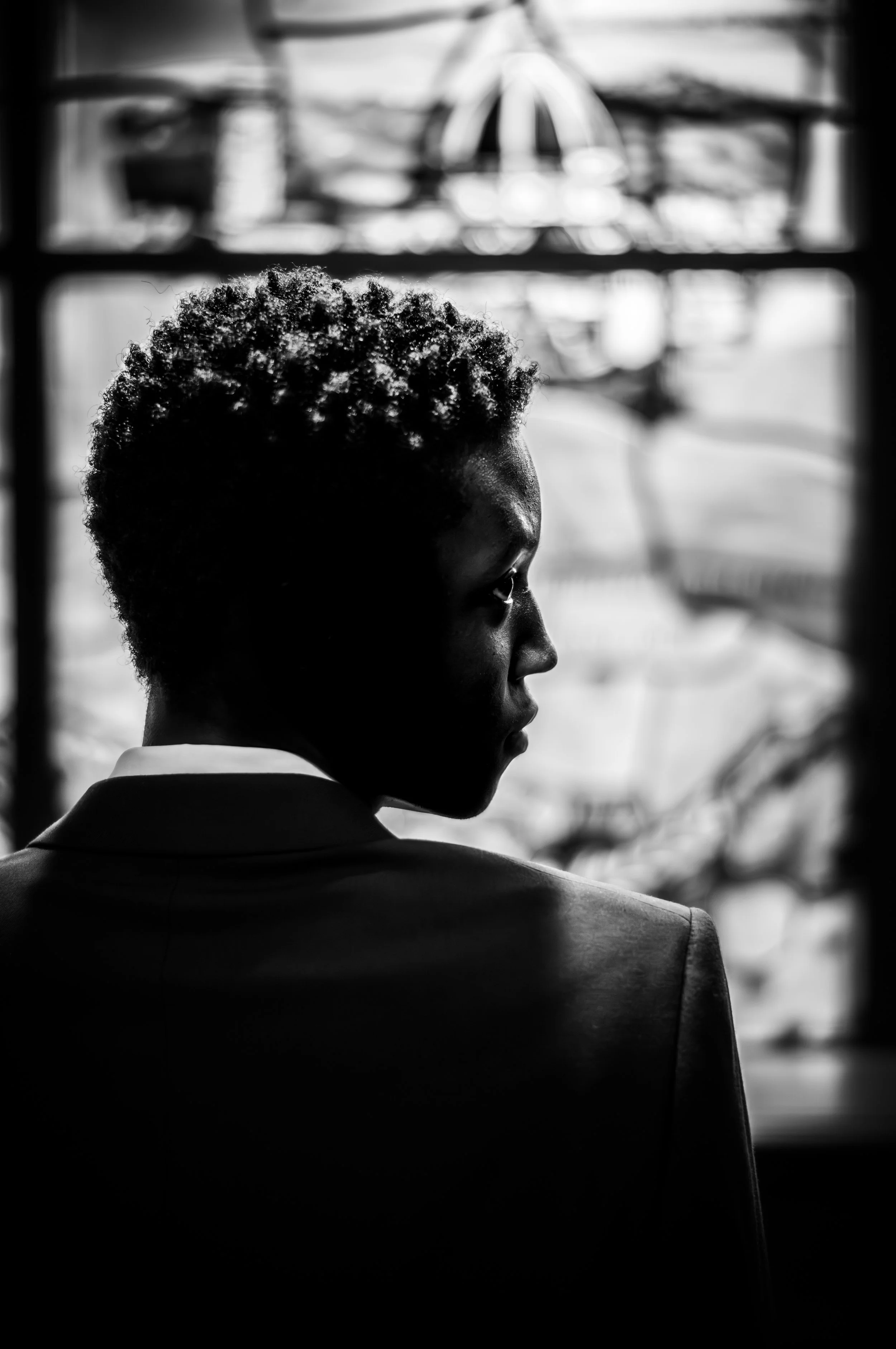 Black and white photo of a person's profile, showing their face in side view and curly hair, with a blurred carnival ride in the background.
