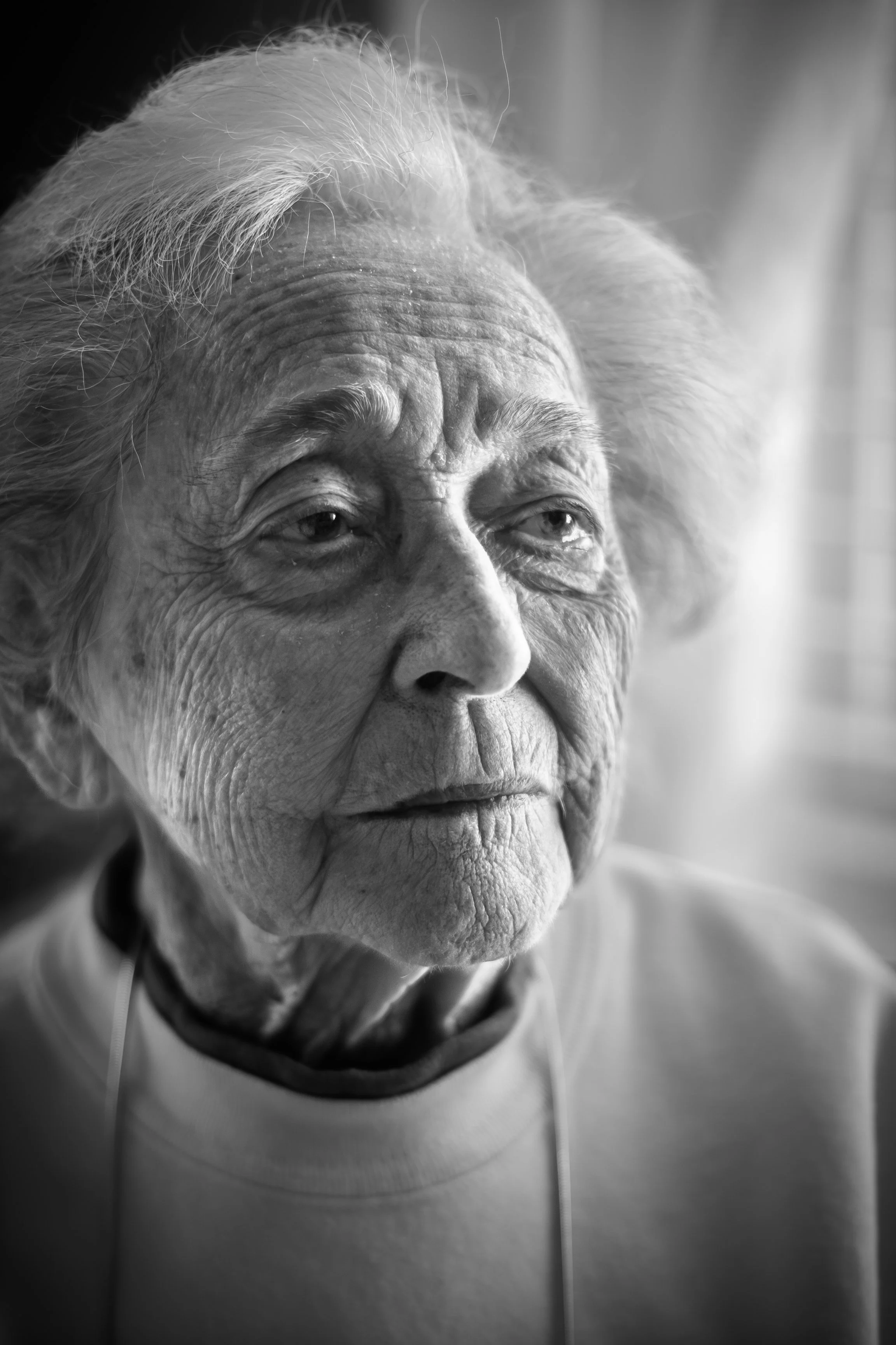 Close-up black and white photo of an elderly woman's face with detailed wrinkles, white hair, and a serene expression.
