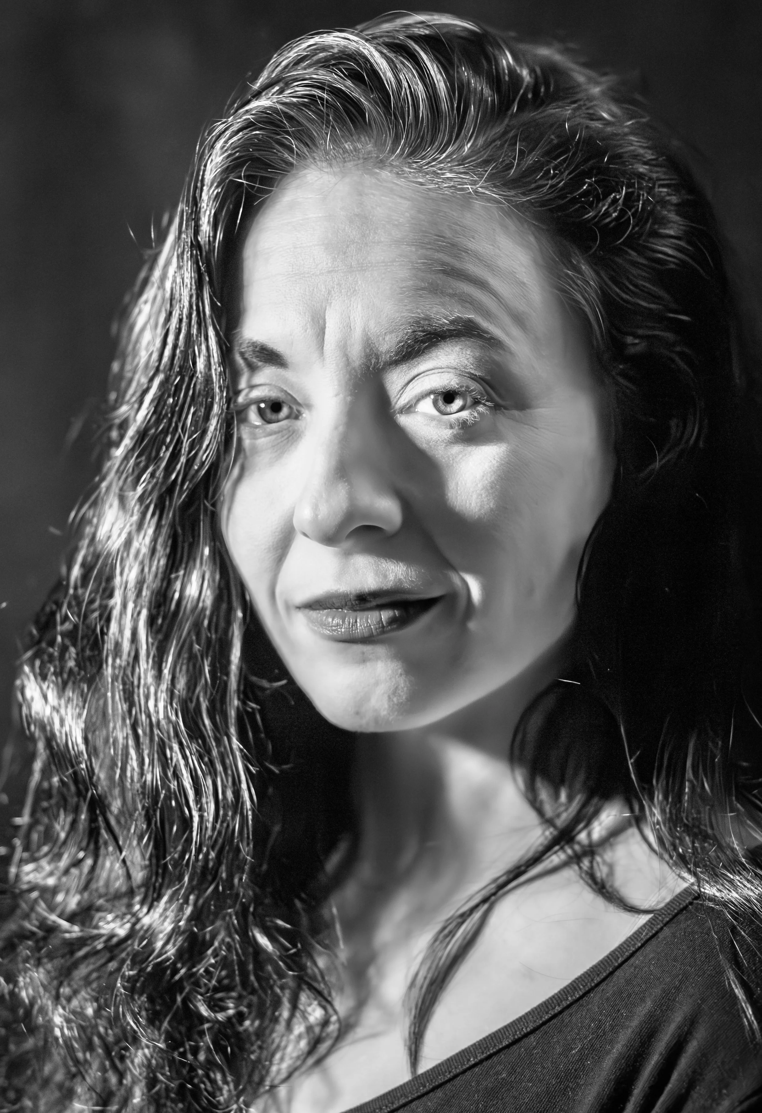 A close-up black and white portrait of a woman with wavy hair, partially crying, with makeup and a dark top.