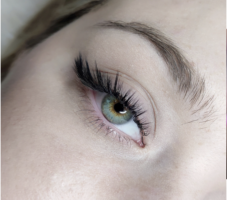 Close-up of a person's green eye with long black eyelashes and well-groomed eyebrows.