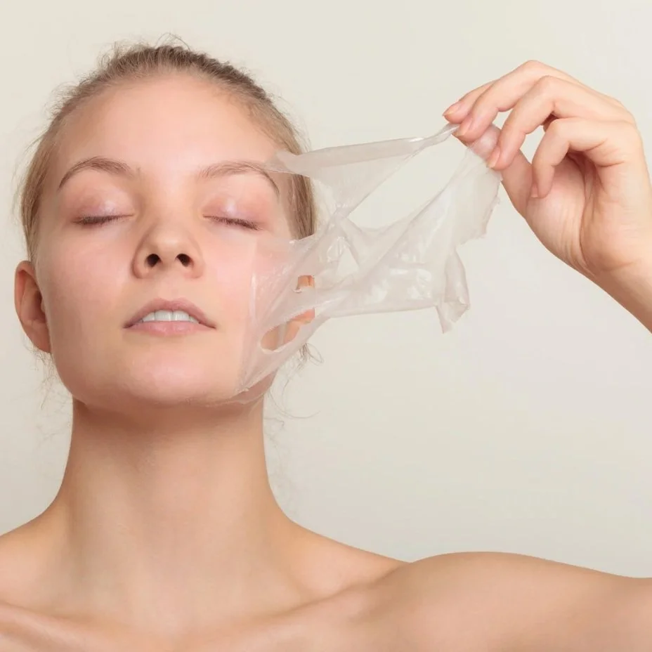 Woman peeling off a facial mask from her face, eyes closed, neutral background
