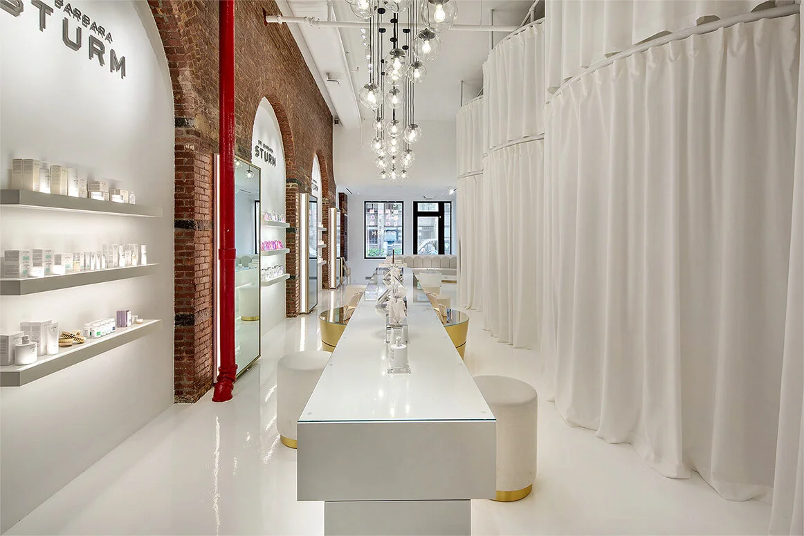 Brightly lit skincare retail space with white floors, floor to ceiling curtains, and table.